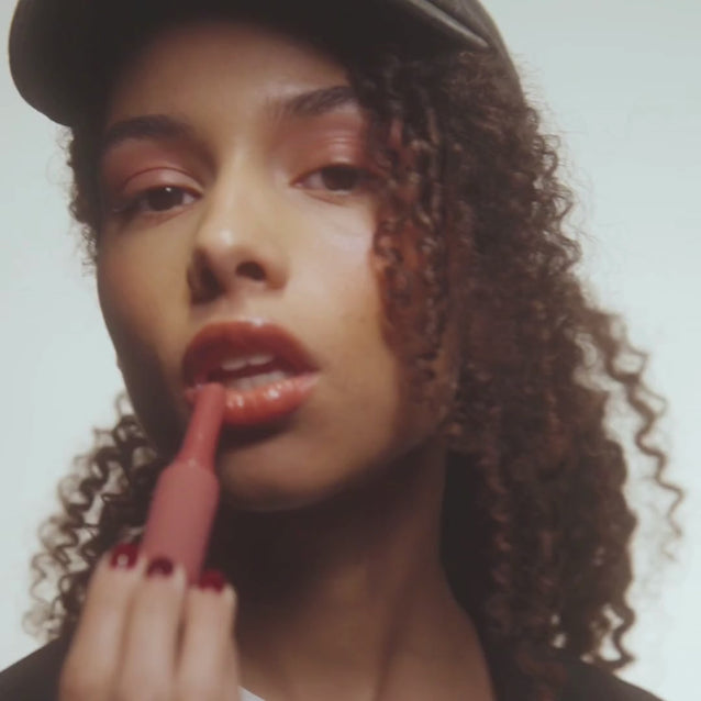 Model using Voice Note Tinted Lip Treatment Balm as a cheek balm and lip tint for a rosy, glossy finish